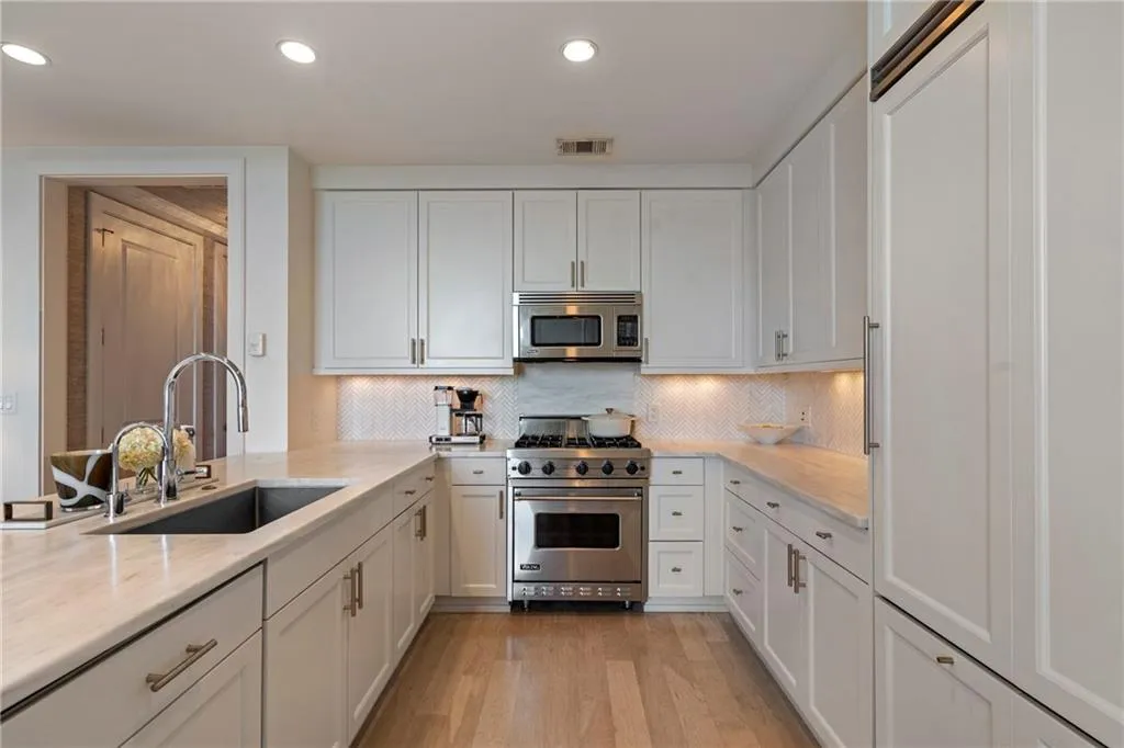 U-shaped kitchen featuring white shaker cabinetry, stainless steel appliances, light-toned countertops, a mosaic tile backsplash, and wood-finish flooring