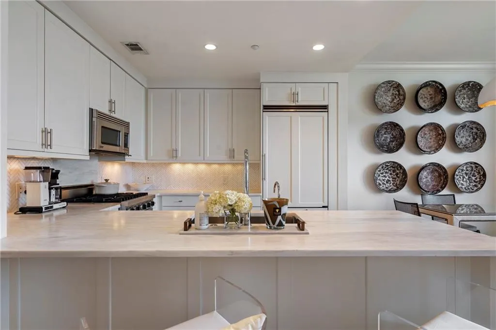 White shaker-style cabinetry with brushed nickel hardware, stainless steel appliances, herringbone tile backsplash, integrated refrigerator, and light-toned countertops