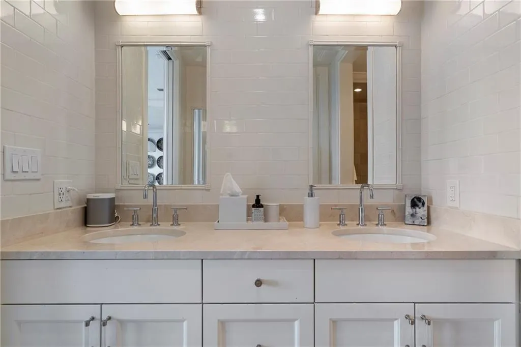 Dual undermount sinks, stone countertop, white shaker-style cabinetry, subway tile backsplash, and individual mirror-front medicine cabinets