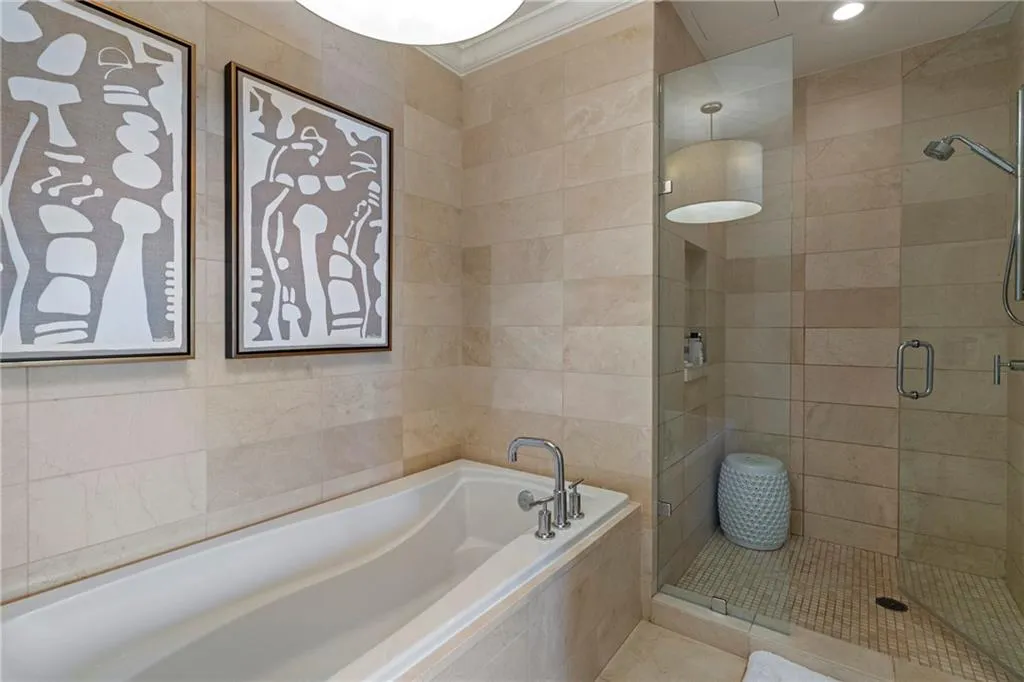 Built-in bathtub with polished chrome fixtures, glass-enclosed shower with tile surround, and recessed lighting