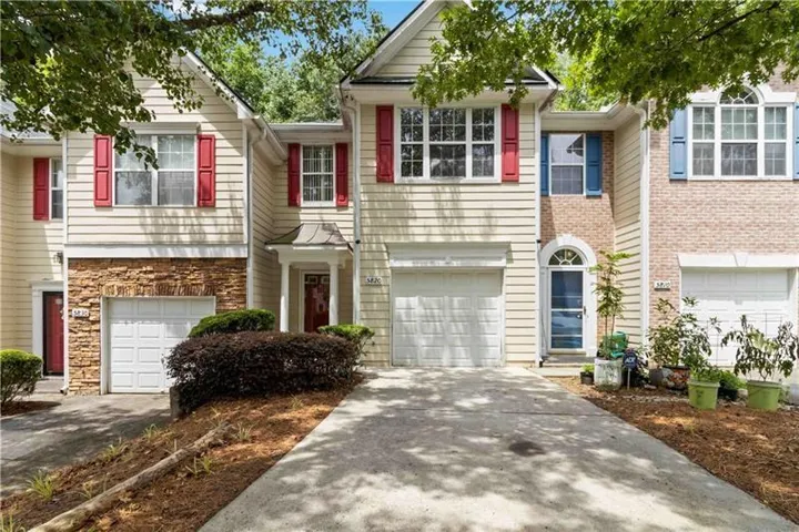 Multi-level townhome featuring a two-car garage, stone facade accents, and vibrant red window shutters