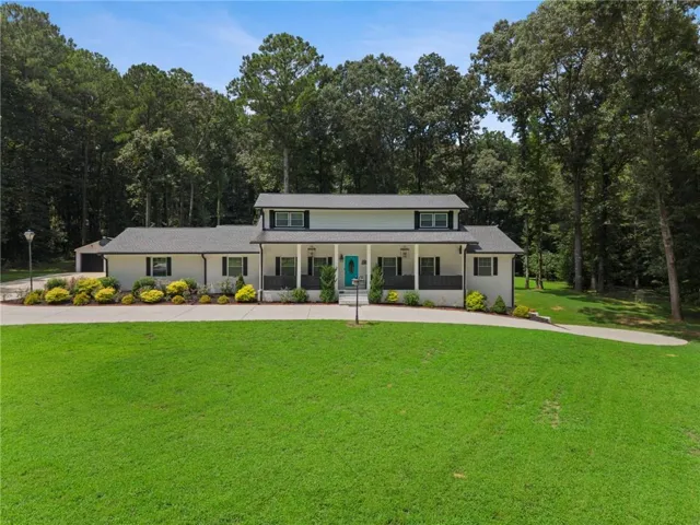 Expansive front lawn, paved drive, mature trees, covered porch, and white exterior with black shutters