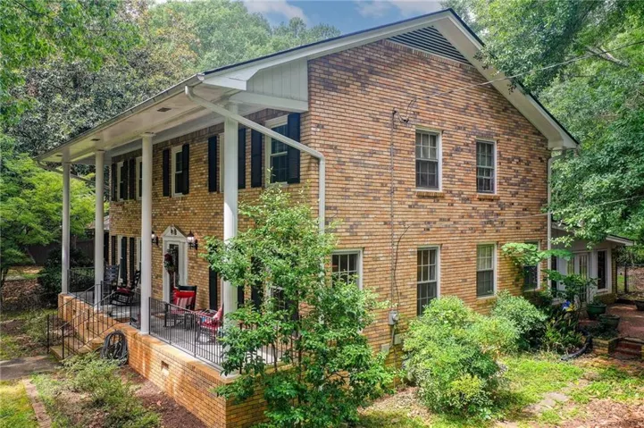 Brick exterior featuring white column supports, black louvered shutters, and a covered porch with a metal railing