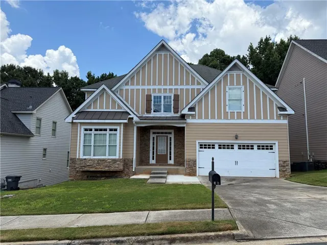 Contemporary home exterior featuring a neutral siding facade with vertical accent panels, a stone accent base, and a two-car garage