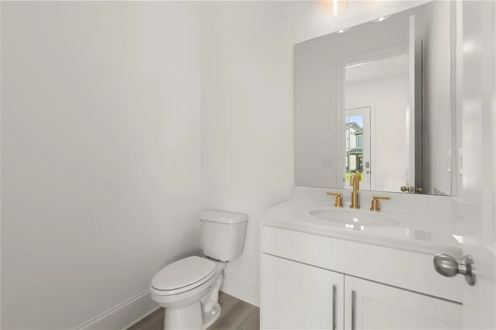 Half bath with toilet, vanity, baseboards, and wood finished floors