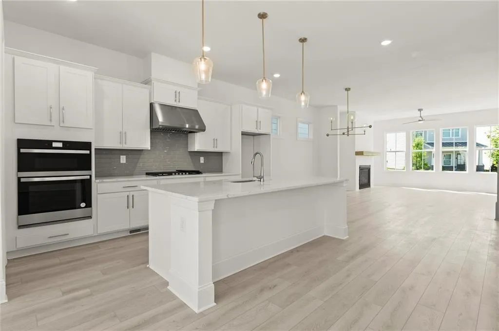 Kitchen featuring under cabinet range hood, a sink, double oven, open floor plan, and light wood-type flooring