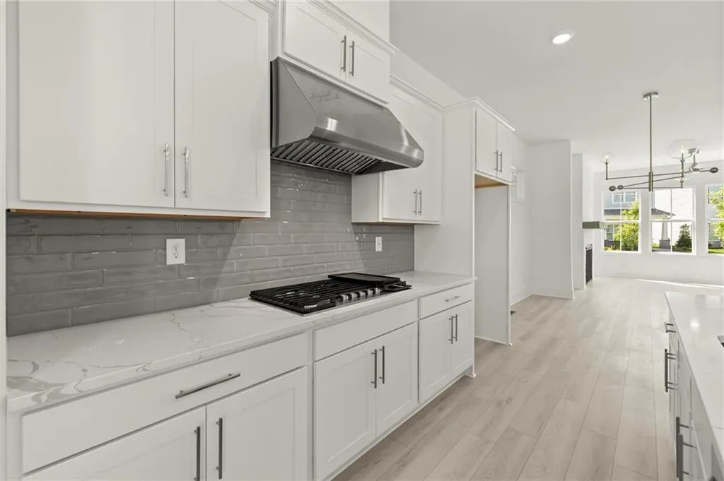Kitchen with under cabinet range hood, stainless steel gas cooktop, white cabinetry, decorative backsplash, and light stone counters