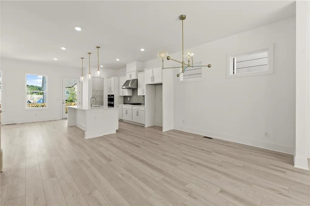 Unfurnished living room with a sink, a chandelier, light wood-type flooring, baseboards, and recessed lighting