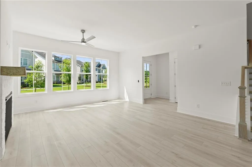 Unfurnished living room featuring ceiling fan, light wood-style flooring, baseboards, and stairway