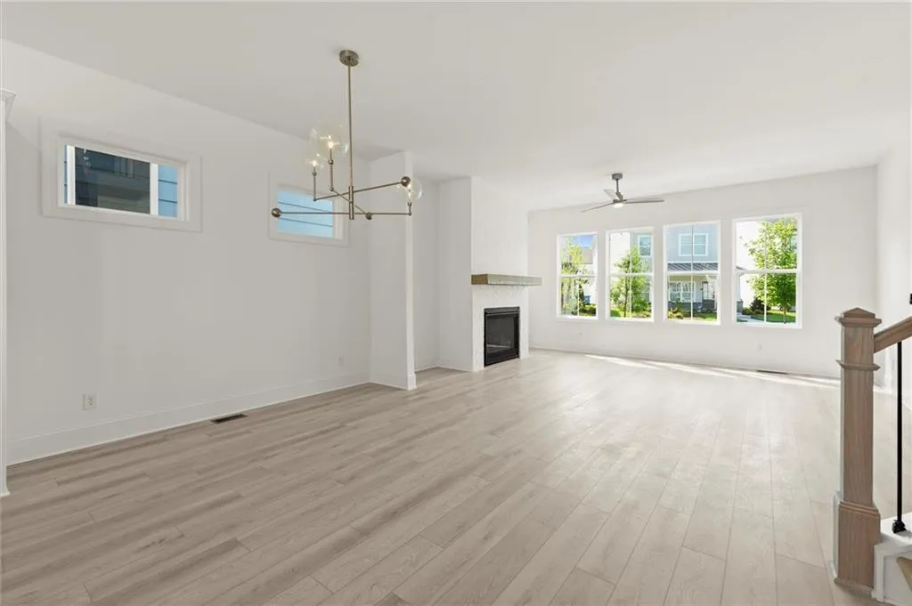 Unfurnished living room with light wood finished floors, a glass covered fireplace, a chandelier, and baseboards