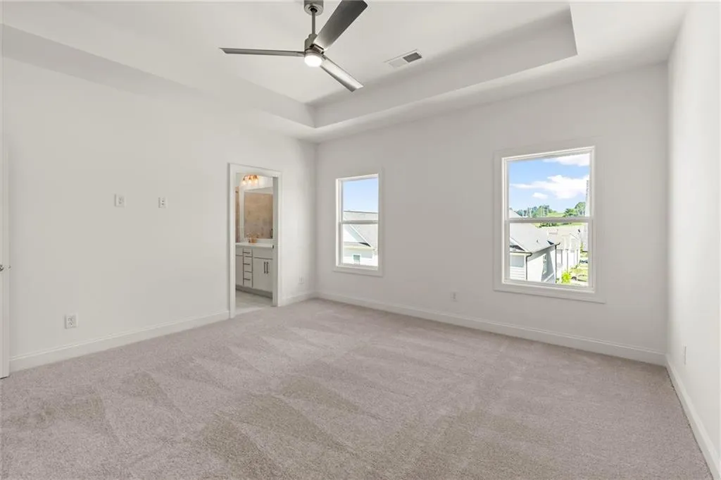 Empty room featuring a tray ceiling, light carpet, a ceiling fan, and baseboards