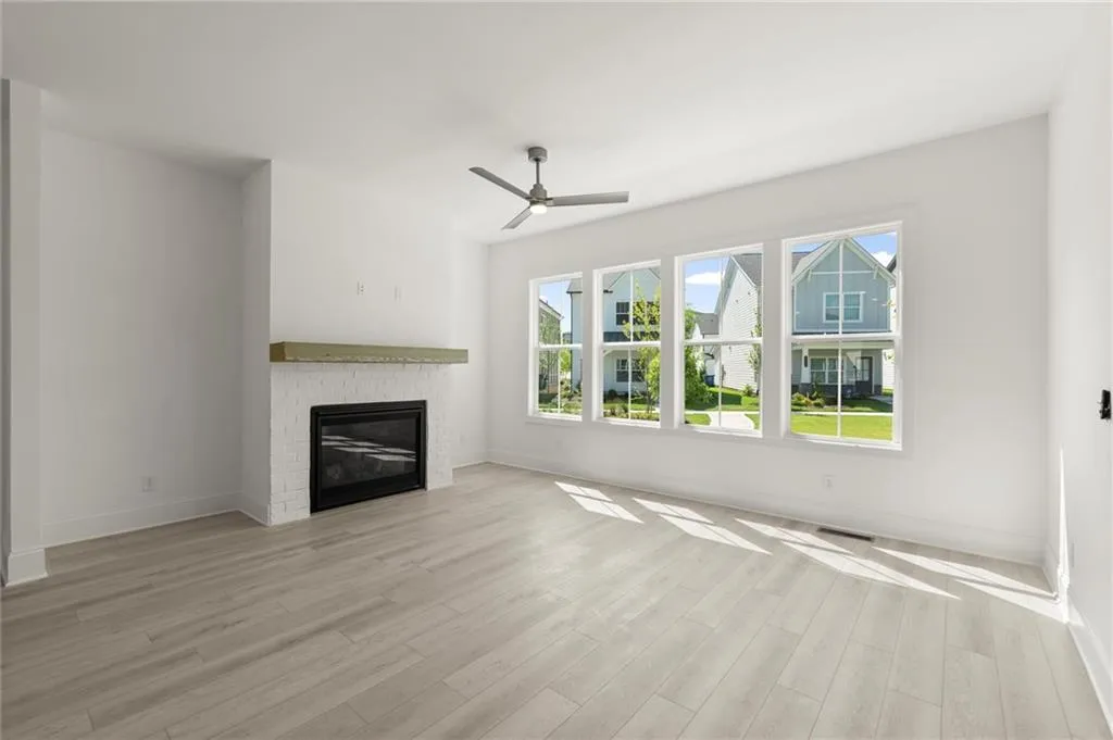 Unfurnished living room with light wood-type flooring, baseboards, a fireplace, and a ceiling fan