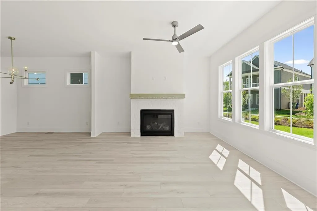Unfurnished living room with light wood finished floors, a ceiling fan, a glass covered fireplace, baseboards, and a chandelier