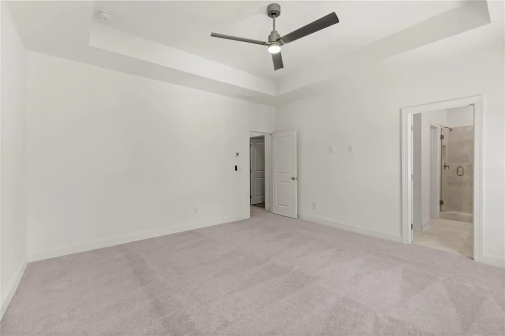 Unfurnished bedroom with a tray ceiling, light carpet, and baseboards