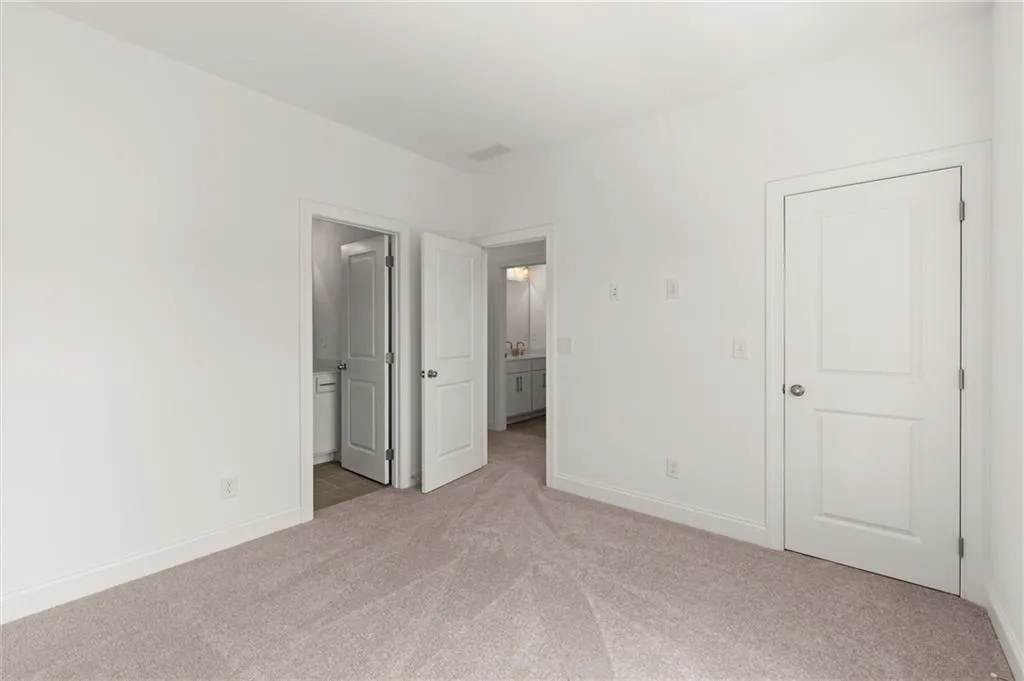Unfurnished bedroom with light colored carpet, baseboards, and ensuite bathroom