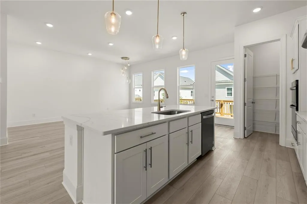Kitchen featuring a sink, dishwasher, light wood-style flooring, an island with sink, and pendant lighting
