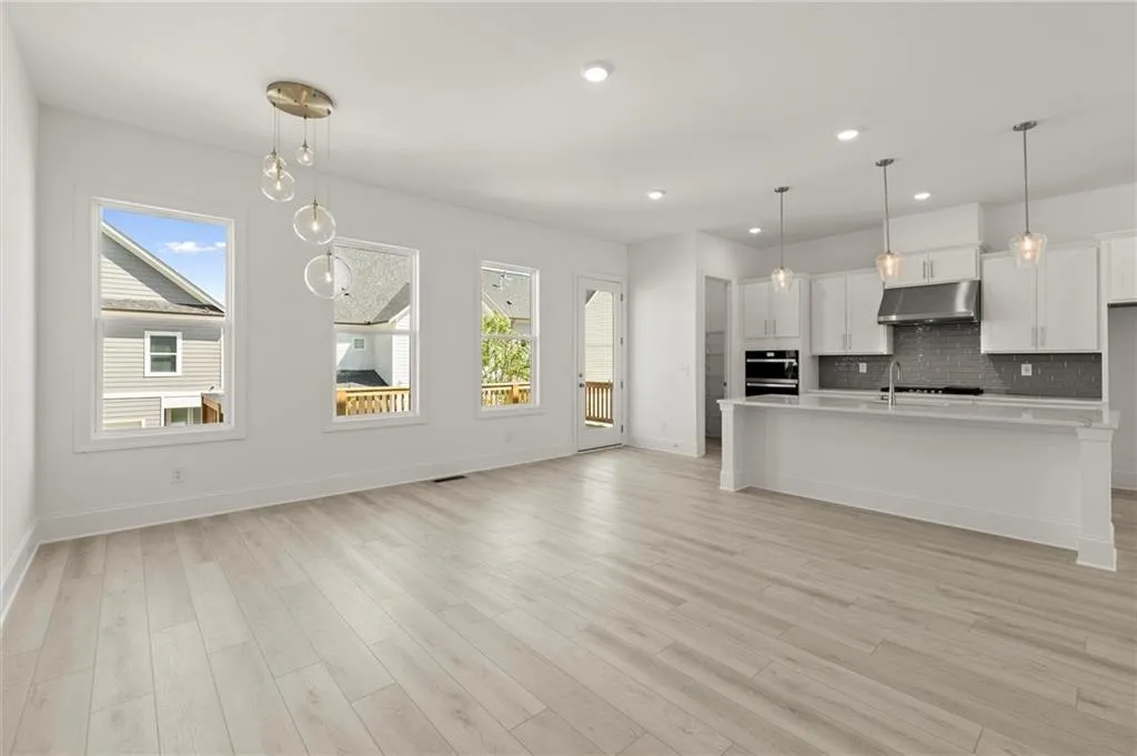 Kitchen with under cabinet range hood, light countertops, decorative backsplash, white cabinets, and baseboards