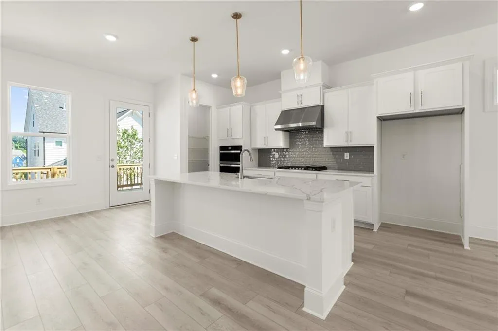 Kitchen featuring under cabinet range hood, a sink, white cabinets, light wood-style flooring, and recessed lighting