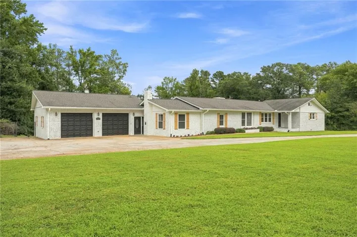 White brick exterior with wood shutters, attached two-car garage, covered entry, and expansive green lawn