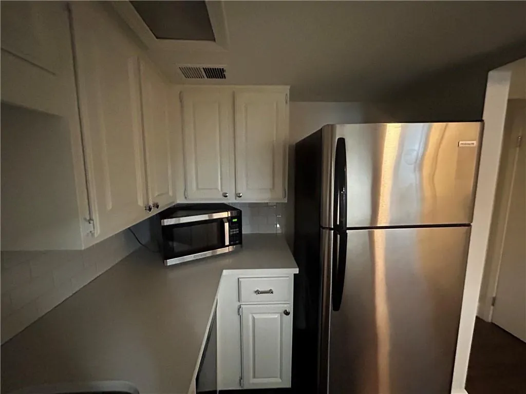 Kitchen featuring stainless steel appliances, white cabinets, backsplash, and light countertops