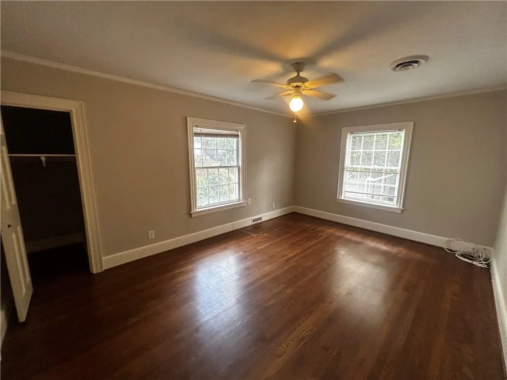 Unfurnished bedroom with ornamental molding, dark wood-style floors, multiple windows, a spacious closet, and a ceiling fan