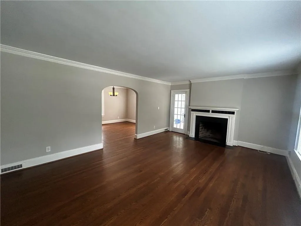 Unfurnished living room featuring crown molding, arched walkways, a fireplace with flush hearth, and dark wood finished floors