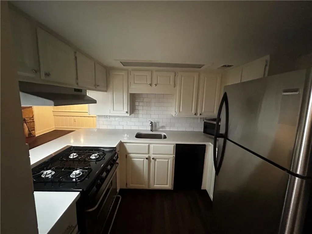 Kitchen with black appliances, tasteful backsplash, dark wood-style floors, and under cabinet range hood
