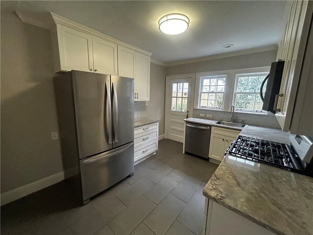 Kitchen with stainless steel appliances, ornamental molding, white cabinetry, light stone counters, and decorative backsplash
