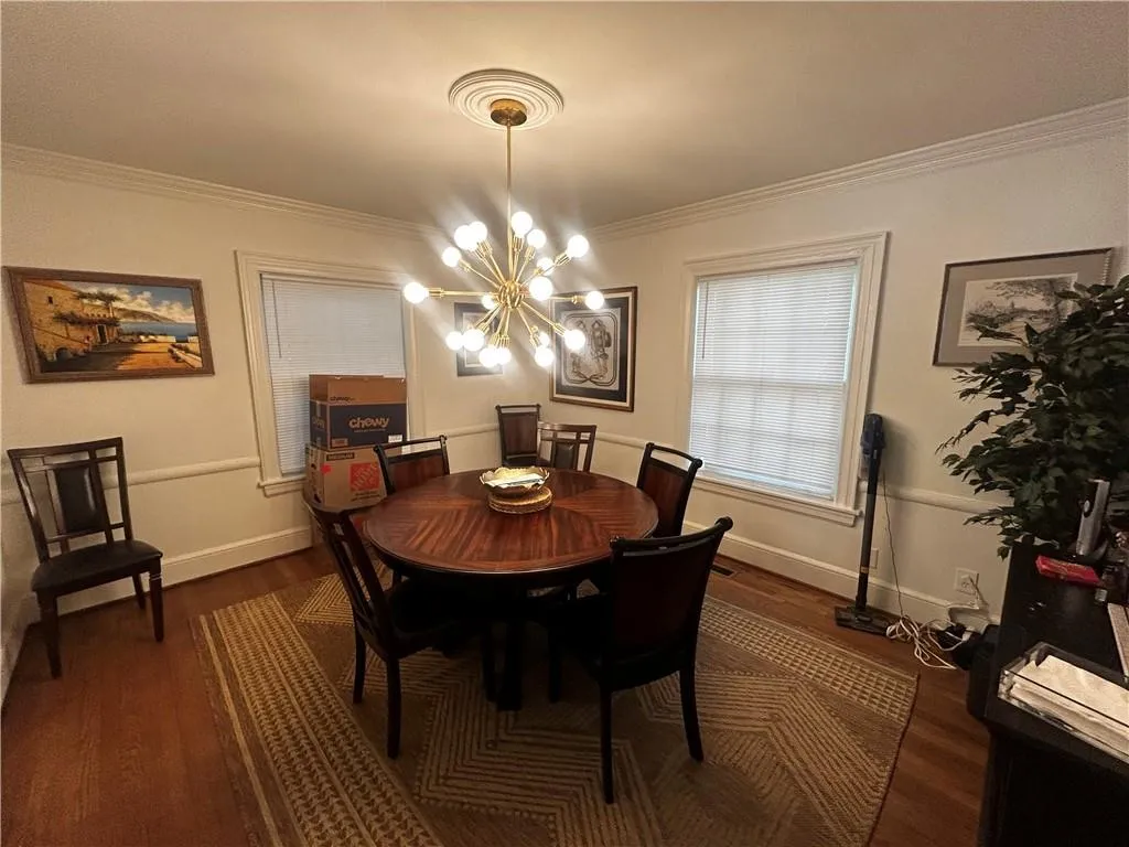 Dining space with dark wood-style flooring, ornamental molding, and a chandelier