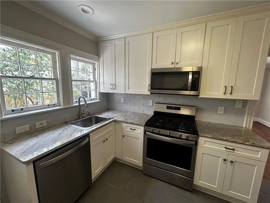 Kitchen with stainless steel appliances, light stone counters, tasteful backsplash, white cabinets, and dark tile patterned floors