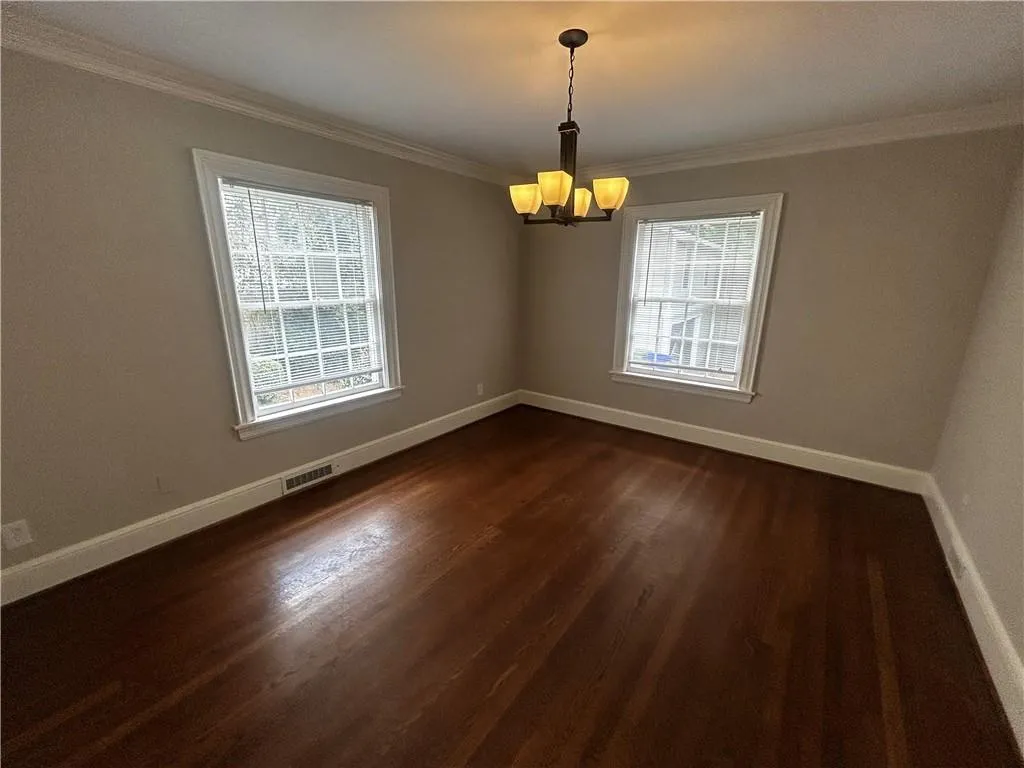 Empty room featuring dark wood-type flooring, crown molding, and a chandelier