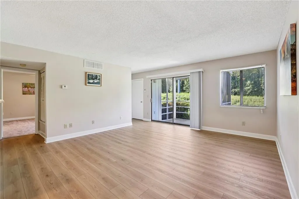 Living room with a textured ceiling and light wood-style flooring with view to woods
