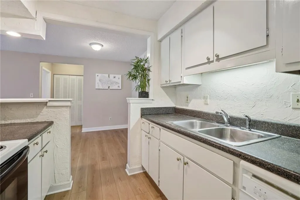Kitchen featuring a textured ceiling, white cabinetry, light wood-style flooring, white appliances, and dark countertops