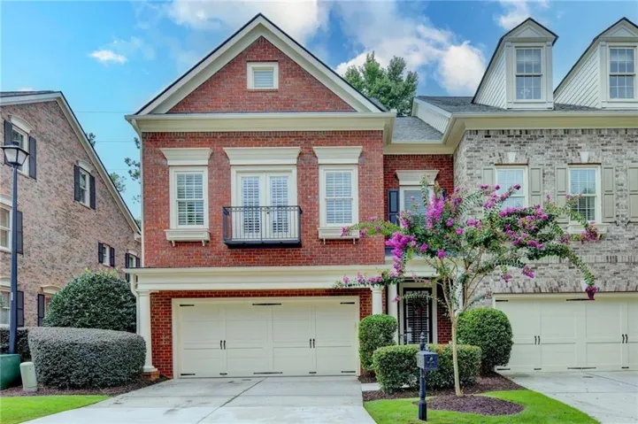 Brick End Unit with private balcony, two-car garage, manicured shrubbery, and a mature flowering tree