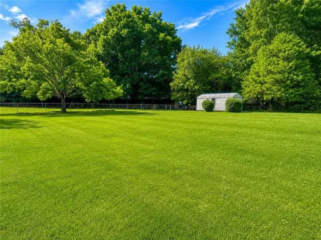 Expansive green lawn with mature trees and a storage shed