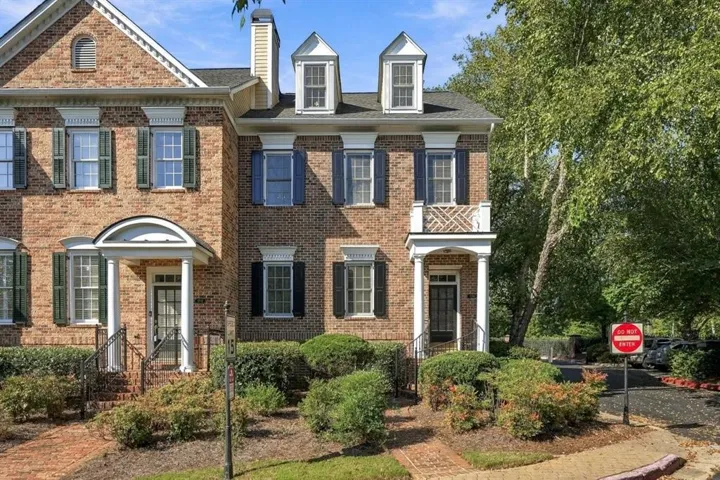 Brick exterior with contrasting shutters, covered entry porch, second-story balcony, and multiple dormer windows