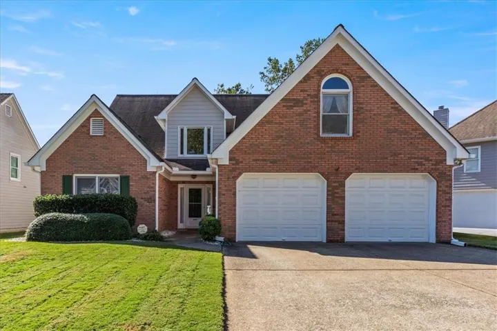 Traditional-style home featuring a front yard, driveway, brick siding, and a garage