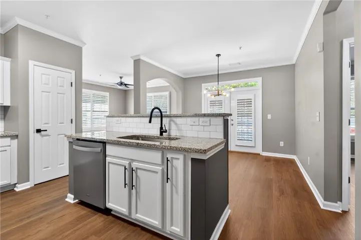 Kitchen with backsplash, a center island with sink, light stone countertops, ornamental molding, and white cabinets