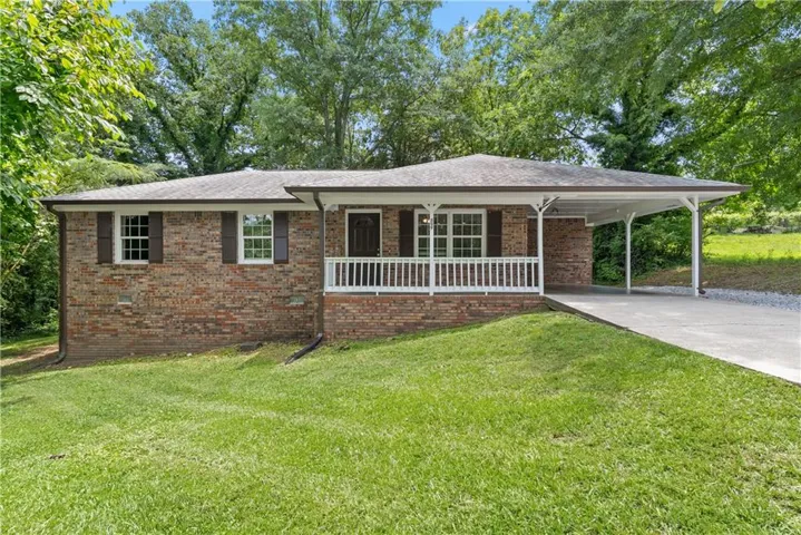 Brick facade property featuring a covered front porch with white railing, a two-car carport, a paved driveway, and mature landscaping