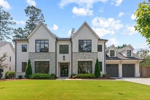 Contemporary two-story residence featuring white siding, stone accents, black-framed windows, a prominent gable roofline, and a three-car garage with dormer windows