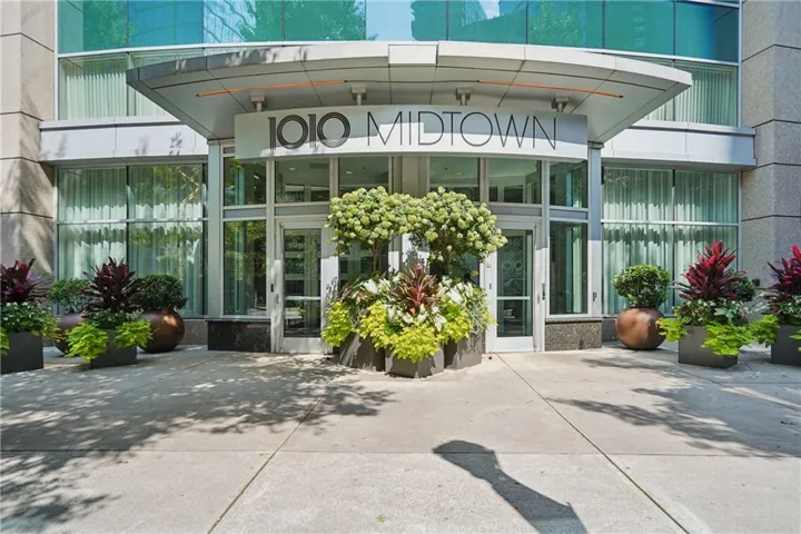 Modern building entrance with curved canopy, glass doors, and structured landscaping