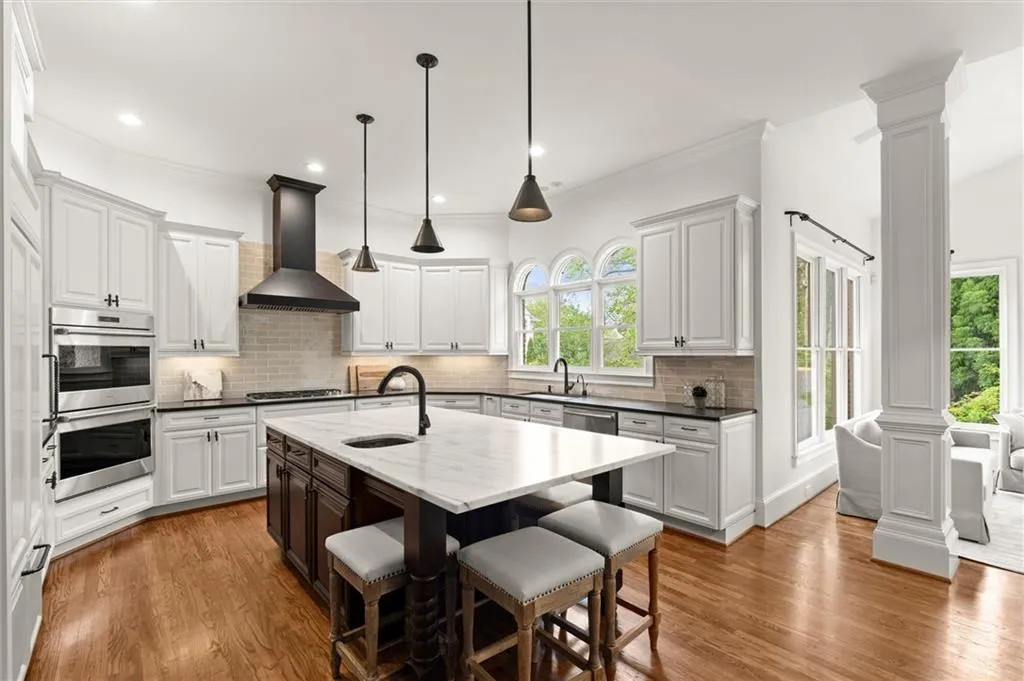 Two tone kitchen with decorative columns, a kitchen bar, stainless steel appliances, dark wood-type flooring, and two tone cabinets