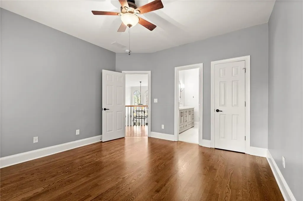 Unfurnished bedroom featuring ensuite bathroom, dark wood-type flooring, and a ceiling fan