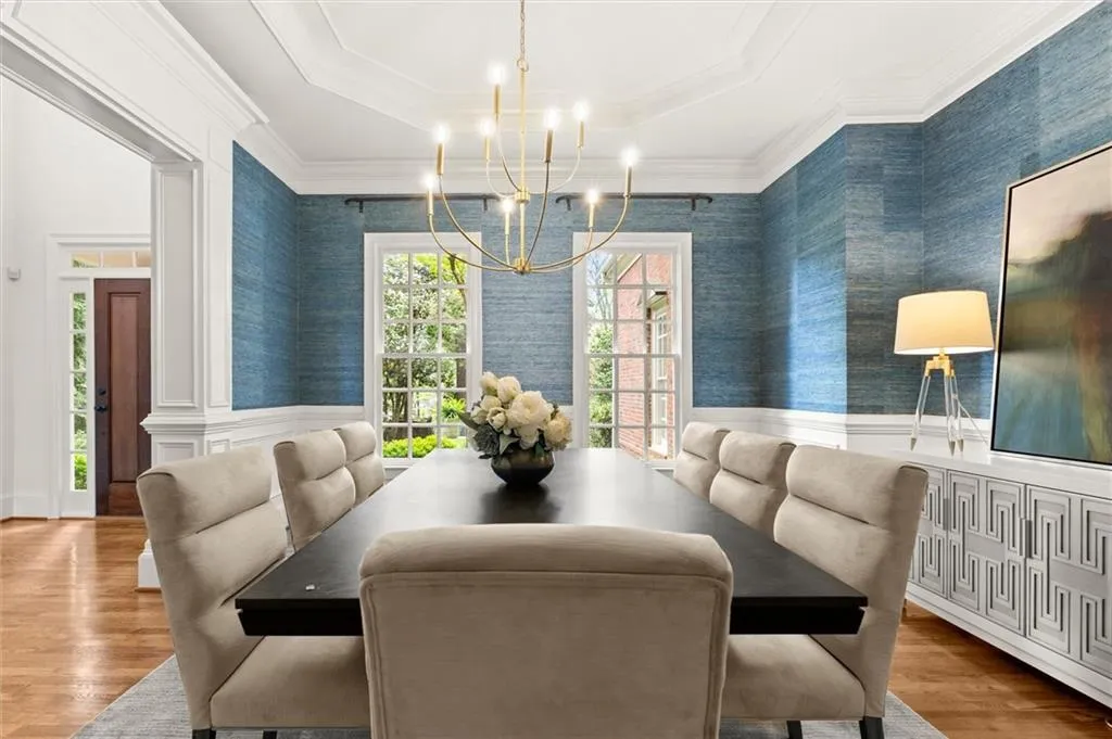 Dining space with wallpapered walls, light wood-type flooring, a chandelier, a wainscoted wall, and a tray ceiling
