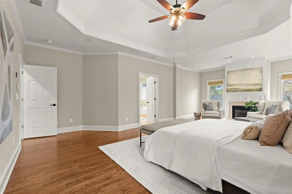 Bedroom with a glass covered fireplace, wood finished floors, crown molding, ceiling fan, and a raised ceiling