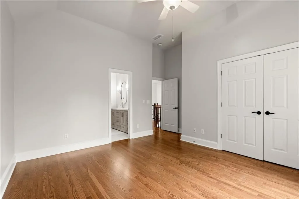 Unfurnished bedroom with a closet, a ceiling fan, wood finished floors, vaulted ceiling, and ensuite bathroom