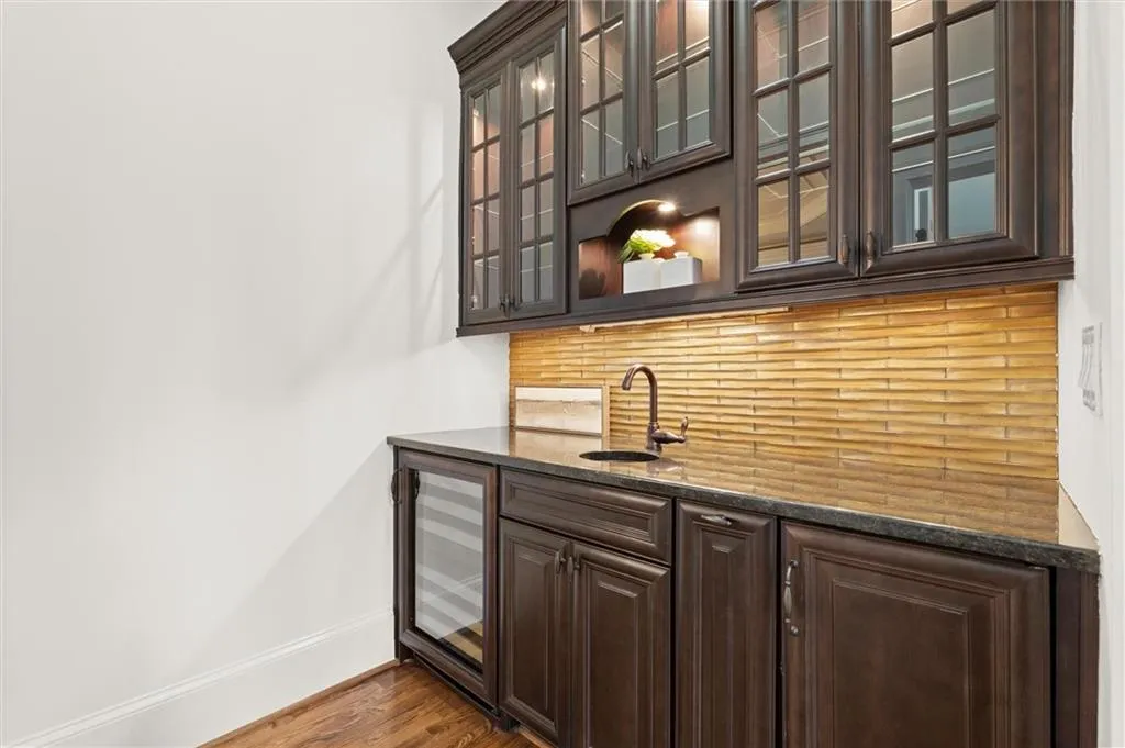 Indoor wet bar with dark wood finish cabinetry, dark stone counters, glass fronted cabinets, beverage cooler, and wood finished floors