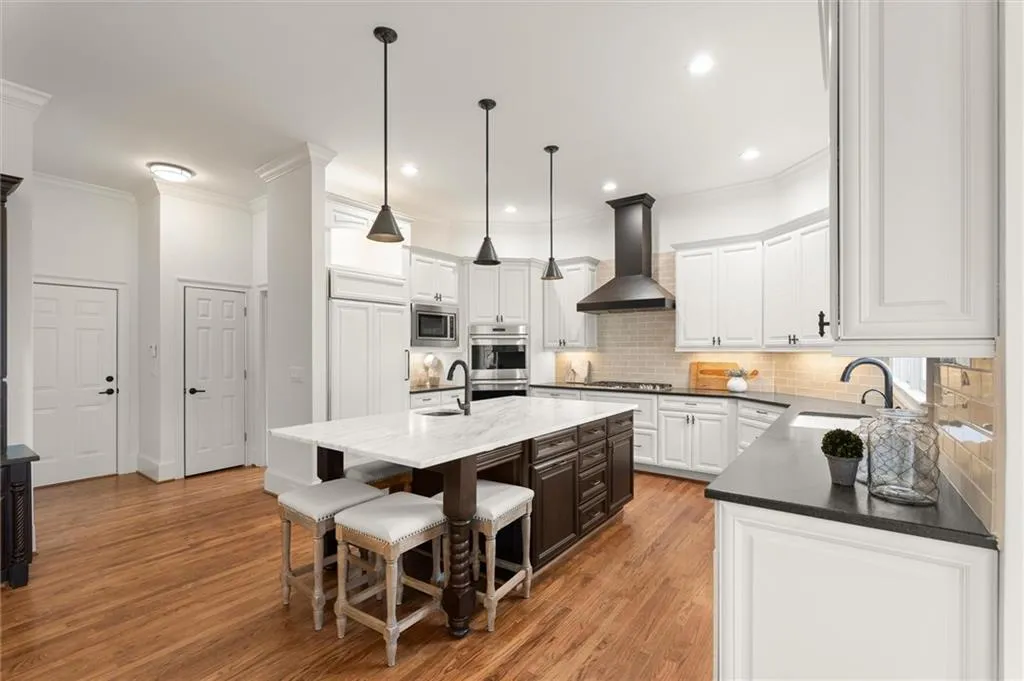 Two tone kitchen featuring crown molding, dual tone cabinetry, a breakfast bar, light wood-type flooring, and dark stone countertops