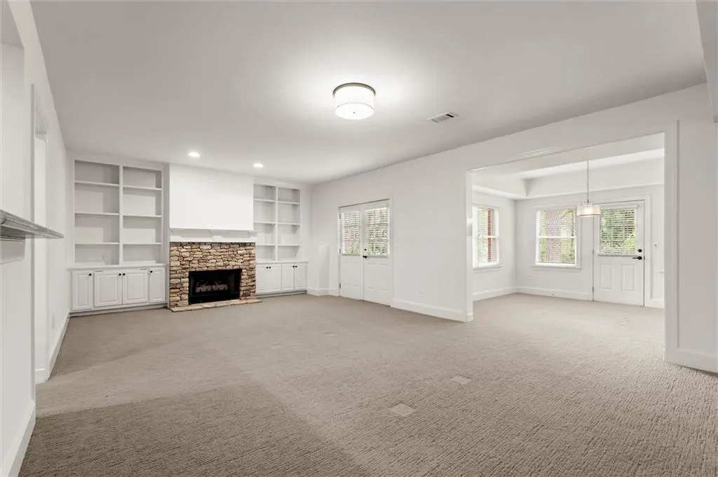 Unfurnished living room with a stone fireplace and light colored carpet