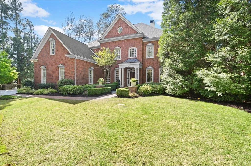 Colonial house featuring a front yard, a chimney, brick siding, and roof with shingles